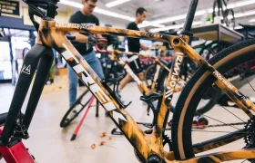 Un mecánico trabaja en una bicicleta TREK naranja en el interior de una tienda de bicicletas, con herramientas en el suelo y otras bicicletas al fondo, capturando una escena que recuerda a States of Elevation, la pasión de Kilian Jornet por los equipos afinados.
