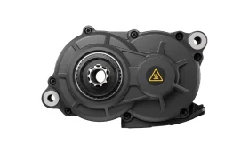Primer plano de una carcasa de engranaje mecánico Avinox M2S negra con un engranaje metálico central y un símbolo de advertencia amarillo en el lado derecho, aislado sobre fondo blanco.
