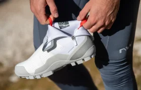 Primer plano de una persona que se ajusta la cremallera de unas zapatillas deportivas blancas y grises mientras lleva unos leggings grises al aire libre.