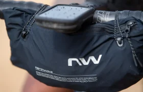 Un primer plano de una bolsa negra para manillar de bicicleta de la marca Northwave con letras blancas, fijada al manillar, con un smartphone colocado encima, en el que se ven gotas de agua sobre el teléfono.