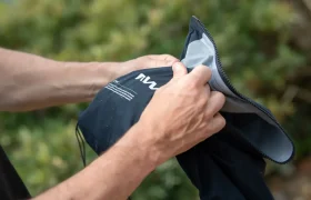 Una persona abre una bolsa negra impermeable con cremallera, dejando al descubierto su interior gris; al fondo se divisa una vegetación difusa.
