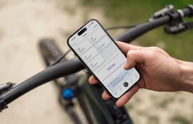 Una persona sostiene un smartphone que muestra una aplicación relacionada con el ciclismo mientras agarra el manillar de una bicicleta al aire libre, demostrando cómo la Bosch Performance Upgrade mejora tu experiencia en bici con mayor potencia.