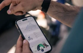 Una persona sostiene un smartphone que muestra una aplicación de seguimiento de la forma física con estadísticas de ciclismo, un gráfico y una imagen de un ciclista, mostrando la actualización Bosch Performance Upgrade para más potencia y mejor experiencia sobre la bici.