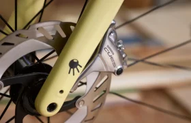 Primer plano de una rueda delantera de bicicleta con una pinza de freno de disco Shimano CUES, grupos de carretera, unida a una horquilla amarilla y un rotor de freno plateado.