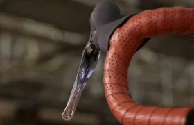 Primer plano de un manillar de bicicleta de carretera envuelto en cinta perforada marrón, con una palanca de freno Shimano CUES negra y plateada.