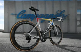 Una bicicleta de carretera de alta gama con ruedas de sección profunda está estacionada afuera de un edificio con "Campagnolo" escrito en letras grandes.