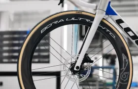 Primer plano de la sección delantera de una bicicleta con cuadro blanco y azul y ruedas Campagnolo Bora Ultra WTO en un entorno interior.