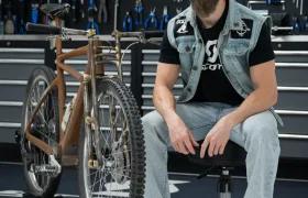 Una persona vestida informalmente se sienta en una silla junto a una bicicleta SCOTT Solace, rodeada por el caos creativo de su taller, con herramientas alineadas en la pared.