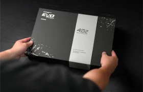 Una persona sostiene una caja rectangular negra con la inscripción «EVO Pro Limited», junto con «4OZ» y elementos decorativos de salpicaduras de pintura blanca: se trata de la TRP EVO PRO Anniversary Edition, una edición limitada exclusiva, expuesta sobre una superficie oscura.