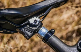Primer plano de un sillín y una tija de sillín de bicicleta con tija telescópica inalámbrica RAGE Circuit, con mecanismo electrónico de tija telescópica, sobre un fondo natural difuminado.