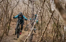 Dos ciclistas de montaña recorren un sendero forestal, con el ciclista que va en cabeza levantando la rueda delantera del suelo gracias a una tija telescópica inalámbrica RAGE Circuit y el segundo ciclista siguiéndole de cerca.