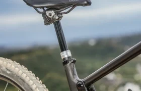 Primer plano de la rueda trasera, la tija del sillín y el sillín de una bicicleta de montaña equipada con una tija telescópica inalámbrica RAGE Circuit, con un paisaje exterior borroso de fondo.