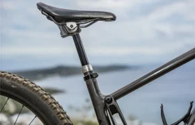 Primer plano de un sillín negro de bicicleta de montaña, tija telescópica inalámbrica RAGE Circuit, y cuadro con un paisaje exterior borroso de fondo.