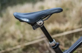 Primer plano de un sillín de bicicleta Ergon negro montado en una tija telescópica inalámbrica RAGE Circuit, con un fondo borroso al aire libre.