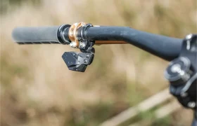 Primer plano de un manillar de bicicleta con un componente electrónico montado, una empuñadura texturizada y la elegante tija telescópica inalámbrica RAGE Circuit, sobre un fondo exterior difuminado.
