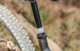 Primer plano de un sillín de bicicleta de montaña, una tija de sillín y un neumático trasero con una tija telescópica inalámbrica RAGE Circuit, sobre un fondo natural al aire libre.