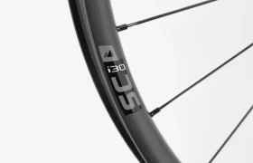 Primer plano de una llanta de bicicleta negra con la etiqueta «i30 SLC» y los radios visibles sobre un fondo blanco liso.