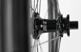 Primer plano de un buje de rueda de bicicleta con la inscripción «X-300» y radios que se extienden radialmente, fotografiado en blanco y negro.