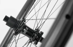 Primer plano en blanco y negro del buje y los radios de una rueda de bicicleta, en el que se aprecian el eje central, las marcas del buje y los radios tensados unidos a la llanta.