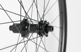 Primer plano de un buje de bicicleta negro con radios que se extienden hacia fuera, sobre un fondo blanco liso.