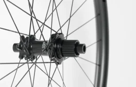Primer plano de un buje de bicicleta negro con radios que se extienden hacia fuera, sobre un fondo blanco liso.