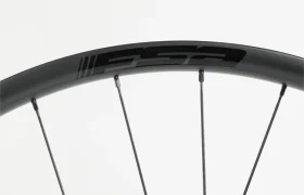 Primer plano de una llanta de bicicleta negra con radios plateados y el logotipo «FSA» impreso en negro en la llanta.