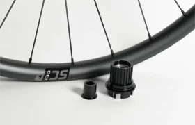 Se muestra una rueda de bicicleta con un primer plano del cuerpo del buje libre y dos adaptadores cilíndricos para el eje sobre un fondo blanco.