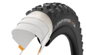 Sección transversal de una cubierta negra para bicicleta de montaña con la inscripción «EMPEROR», en la que se aprecian las capas de su estructura interna y el dibujo de la banda de rodadura, inspirada en neumáticos de MTB de alta gama, como los de la serie Scorpion de Pirelli.