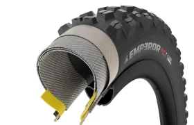 Una sección transversal de una cubierta de bicicleta negra y con protuberancias, con la inscripción «EMPEROR SOFT», muestra las capas internas y los detalles de su construcción, lo que recuerda el diseño robusto de los neumáticos Pirelli Scorpion para MTB.