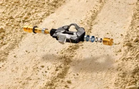 Se muestra un pedal de bicicleta en un entorno arenoso, con sus componentes internos dispuestos en un despiece, destacando los pedales Gravel diseñados para encajar perfectamente en el ecosistema LOOK.
