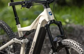 Una bicicleta de montaña eléctrica Focus blanca, de la gama FOCUS e-MTB 2027, con suspensión delantera, está aparcada en un sendero forestal.