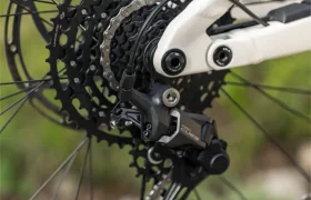 Primer plano del cambio trasero, el cassette y la cadena de una bicicleta eléctrica de montaña Gama FOCUS 2027 de color blanco, con el disco de freno y un fondo verde difuminado.