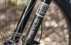 Primer plano de una horquilla de suspensión delantera de bicicleta de montaña con la inscripción «RockShox PsylO», con un freno de disco y un neumático Maxxis visibles al fondo, similares a los componentes de alto rendimiento que incorpora la bicicleta eléctrica de montaña Gama FOCUS e-MTB 2027.