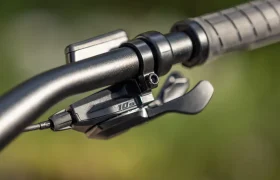 Primer plano del manillar de una bicicleta eléctrica de montaña (e-MTB) de la marca FOCUS, en el que se aprecia una palanca de cambio con la inscripción «10s» y un puño texturizado, sobre un fondo verde difuminado.