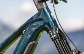 Primer plano del manillar, la horquilla de suspensión delantera y el cuadro de una bicicleta de montaña eléctrica FOCUS e-MTB 2027 de color verde oscuro —posiblemente un modelo SAM o JAM— con un fondo al aire libre difuminado.