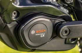 Primer plano de un motor para bicicleta eléctrica Bosch Performance Line CX montado en un cuadro negro de e-MTB 2027, con césped visible al fondo.