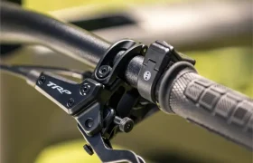 Primer plano de una palanca de freno TRP y una empuñadura en el manillar de una bicicleta eléctrica de montaña SAM 2027, con un fondo verde difuminado.