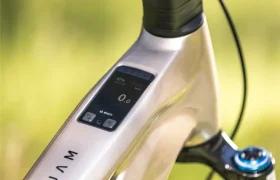 Primer plano del cuadro metálico de una bicicleta eléctrica de montaña JAM e-MTB 2027, con una pantalla digital integrada en el tubo superior, manillar negro y suspensión delantera visible, sobre un fondo difuminado al aire libre.