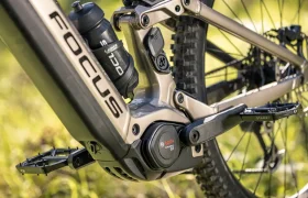 Primer plano de la transmisión de una bicicleta eléctrica de montaña (e-MTB) SAM 2027, en el que se aprecian el motor Bosch Performance Line CX, la batería, el pedal y el bidón, con un fondo exterior desenfocado.