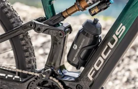 Primer plano del cuadro verde de una bicicleta de montaña Focus —posiblemente de la serie JAM o SAM— en el que se aprecian la suspensión trasera, el portabidones y parte de la transmisión, en un camino de grava.