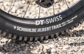 Primer plano de una rueda de bicicleta con neumático Schwalbe Albert Trail y llanta DT Swiss sobre terreno de grava, incorporada en la innovadora e-MTB JAM 2027.