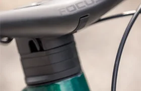Primer plano del cuadro delantero y el manillar de una bicicleta, en el que se aprecia el logotipo de Focus y parte de un cuadro de una bicicleta eléctrica de montaña (e-MTB) FOCUS de color verde y blanco, lo que resalta el diseño característico del modelo JAM.