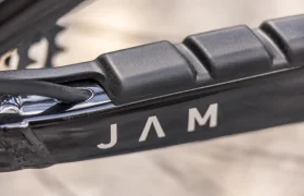 Primer plano del cuadro de una bicicleta eléctrica de montaña (e-MTB) negra del modelo 2027, en el que se ven las letras «JAM» en blanco, junto con parte de un piñón y un cable.