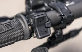 Primer plano del manillar de una bicicleta eléctrica de montaña (e-MTB) FOCUS 2027, en el que se aprecian los puños texturizados, los botones de control electrónico y una palanca de cambios JAM fijada al manillar.