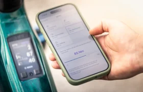 Una mano sujeta un smartphone en el que se muestra un valor de par de 85 Nm, junto a la pantalla montada en el manillar de una bicicleta eléctrica de montaña FOCUS e-MTB 2027.