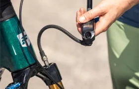 Persona inflando una rueda de bicicleta de montaña con una bomba manual, con el foco en las manos, la bomba y la horquilla de suspensión delantera de una bicicleta eléctrica de montaña Gama FOCUS e-MTB 2027.