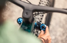 Primer plano de una persona ajustando la suspensión de la horquilla delantera de una bicicleta eléctrica de montaña FOCUS, en el que se ven el manillar y la rueda delantera.