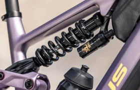 Primer plano del sistema de suspensión trasera de una bicicleta eléctrica de montaña (e-MTB) FOCUS 2027, con un amortiguador de muelle helicoidal y dos bidones de agua montados en el cuadro, que pone de manifiesto la ingeniería de precisión de las series JAM y SAM.