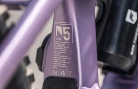 Primer plano del cuadro de una bicicleta morada cerca de la rueda trasera, en el que se aprecian los detalles técnicos «M5» y parte de un bidón negro montado en la bicicleta, que recuerda al elegante diseño de la FOCUS e-MTB 2027.