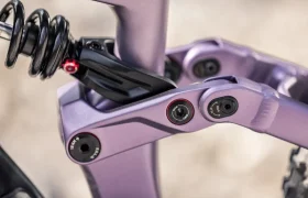 Primer plano del sistema de suspensión trasera de una bicicleta eléctrica de montaña FOCUS e-MTB 2027, en el que se aprecian el amortiguador de muelle helicoidal, los pernos de pivote y un detalle del cuadro en color morado metalizado.